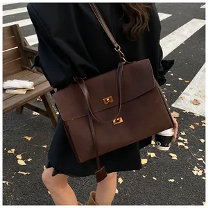Detail of a deep coffee suede tote bag with dual gold twist locks in an autumn setting