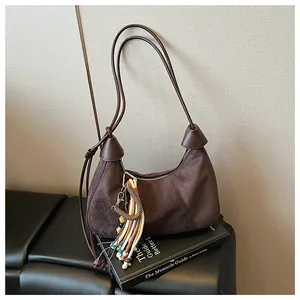 Détail du sac croissant en daim marron foncé avec bandoulière nouée et pompon ethnique