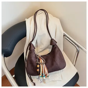 Détail du sac polochon en daim marron avec pendentif à pompons colorés sur une chaise