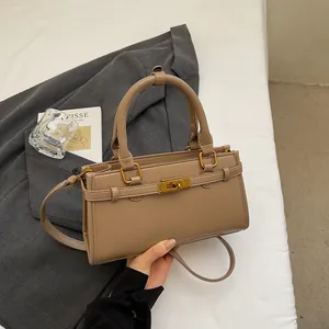 Détail du sac à main kaki avec fermoir doré sur fond de literie blanche et livre d'art