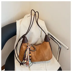 Détail d'un sac hobo en daim marron avec pompon ethnique sur un blazer en velours