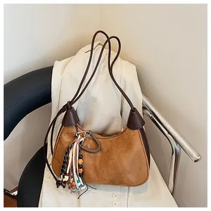 Détail du sac demi-lune en daim fauve avec bordure en cuir et pompon bohème décoratif