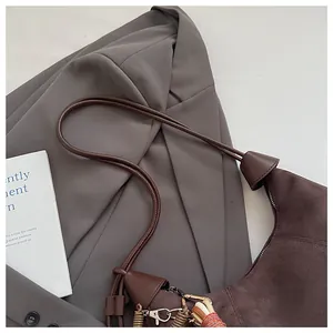 Détail d'un sac hobo en daim marron avec porte-clés à franges sur un blazer gris