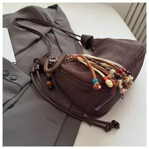 Détail du sac dumpling en daim marron avec pompon ethnique et accents de perles colorées
