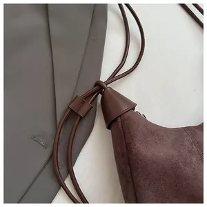 Gros plan détaillé du sac en daim marron foncé avec fine bandoulière et pompons cuir