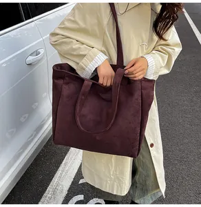 Street style view of a large burgundy suede tote bag worn on the shoulder in a city setting