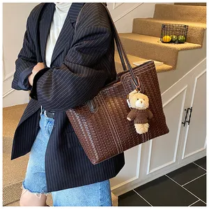 Detail of dark brown woven tote bag with a small bear charm in a chic urban setting
