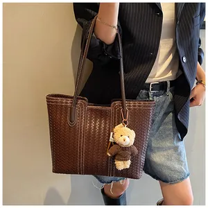 Detail of deep brown woven tote bag featuring diamond textures and a cute bear charm