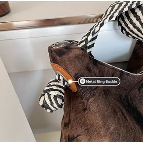 Detail of silver hardware ring and black and white striped rope handle on brown suede bag