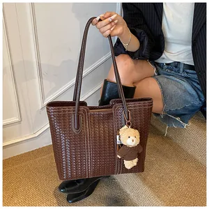 Detail of dark brown woven tote bag with white stitching and bear charm