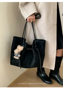 Detailed texture of black suede tote bag with a cute beige plush bear charm accessory