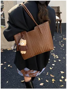Detail of dark brown woven tote bag with white stitching and cute bear charm pendant