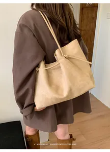 Detailed side view of a large beige suede tote bag with drawstring knots on a model