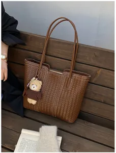 Close-up of brown woven tote bag with a cute bear plush keychain on a park bench