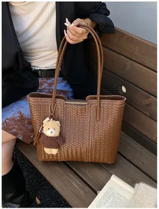 Close-up of brown woven tote bag with bear charm and long handles on a wooden bench