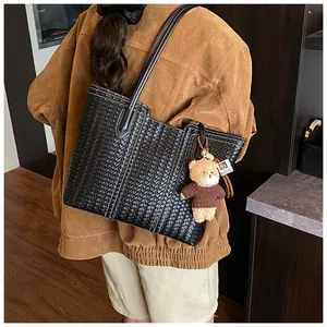 Detail of black woven tote bag with white contrast stitching and a cute bear bag charm