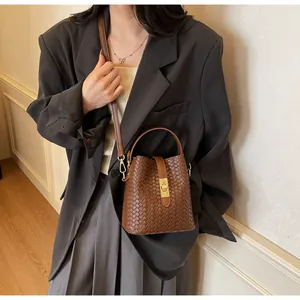 Detail view of brown woven leather bucket bag with retro gold hardware on model