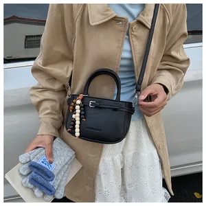 Detail of black PU leather handbag with wooden bead tassel and fashion logo embossing