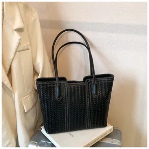 Detail of black woven leather tote bag with white contrast stitching on a suitcase