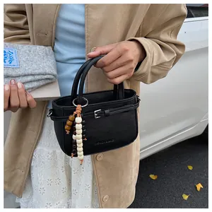 Close-up of black matte leather mini handbag with stylish beaded charm and embossed logo