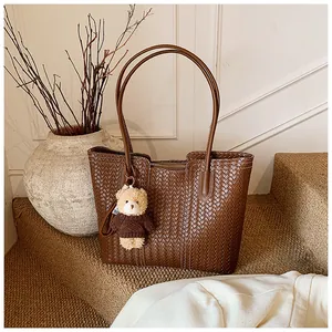 Detail of dark brown woven leather tote bag with round handles and a cute bear keychain charm