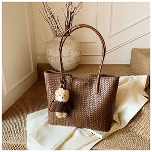 Detail of brown woven leather tote bag with a cute teddy bear charm in warm indoor setting
