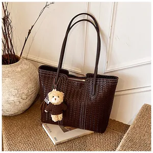 Detailed view of deep brown woven leather tote bag with a cute teddy bear charm