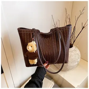 Detail of dark brown woven tote bag featuring white contrast stitching and a teddy bear charm
