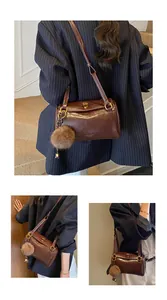 Détail du sac cylindre marron vintage avec charme en peluche et logo sur le cuir