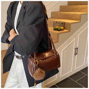 Détail du sac polochon en cuir brillant marron avec fermoir doré et pompon doux