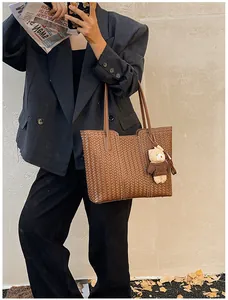 Detail of dark brown woven tote bag featuring a cute teddy bear plush charm and slim strap