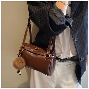 Détail d'un sac cylindrique en cuir marron foncé brillant avec pendentif en peluche doré