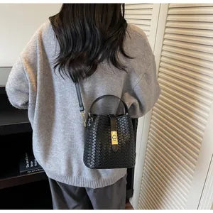 Detailed view of black woven leather bucket bag with gold lock and thin shoulder strap
