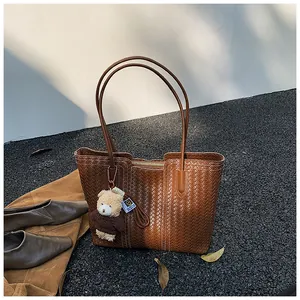 Detailed view of woven brown tote bag with bear charm and fine leather craftsmanship texture