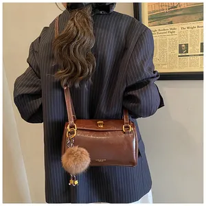 Détail du sac cylindre en cuir marron foncé avec pompon en peluche et bandoulière