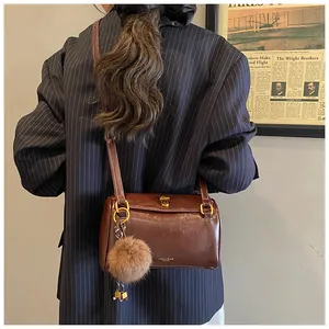 Sac cylindre vintage marron avec fermoir doré et pompon sur une veste de blazer rayée