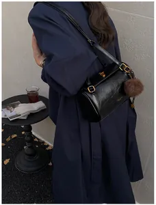 Détail du sac cylindrique noir brillant avec fermoir doré et pompon en fausse fourrure
