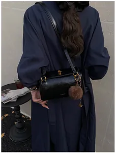 Détail du sac bandoulière cylindrique noir avec boucle dorée et pompon en fausse fourrure