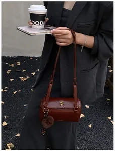 Détail du sac bandoulière cylindrique marron foncé avec boucle bronze et pompon
