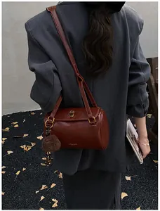 Détail du sac Boston vintage marron foncé avec pompon en peluche porté par le mannequin