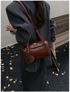 Sac cylindrique en cuir marron avec fermoir doré et pendentif peluche sur bandoulière