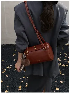 Détail du sac cylindre en cuir marron foncé avec fermoir doré et pompon en peluche