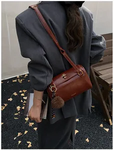 Détail du sac cylindre marron foncé avec fermoir doré et pompon sur veste grise