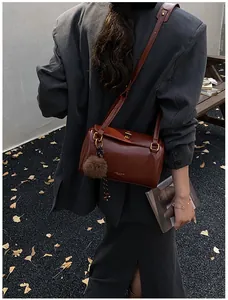 Détail du sac Boston en cuir brillant marron foncé avec fermoir doré et breloque peluche