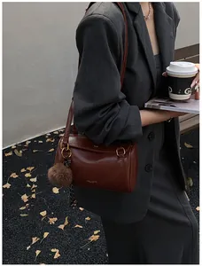 Sac bandoulière cylindrique marron en cuir avec pompon sur fond de style urbain moderne