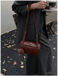 Détail d'un sac cylindre marron vintage avec fermoir doré et pendentif boule en peluche