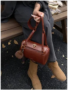 Détail d'un sac cylindrique marron avec un fermoir doré et un pompon en peluche