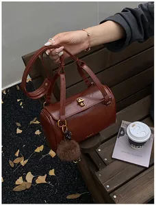 Détail d'un sac cylindre en cuir marron avec fermoir doré et breloque pelucheuse sur banc