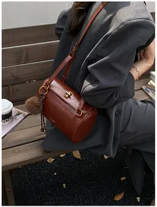 Photo lifestyle d'un sac cylindrique marron avec fermoir doré et pompon en extérieur