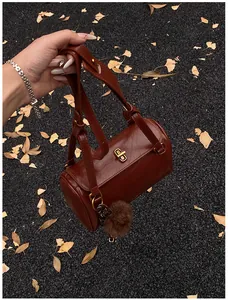 Détail d'un sac cylindre en cuir marron rouge foncé avec serrure dorée et breloque